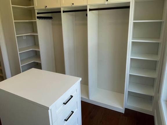Modern walk-in closets with a variety of shelving and hanging rods, with an island of drawers by California Closets Wilmington, North Carolina.