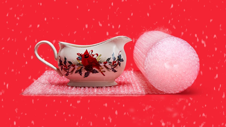 Image of a fragile gravy boat being packaged with bubble cushion on a red background with snow falling.