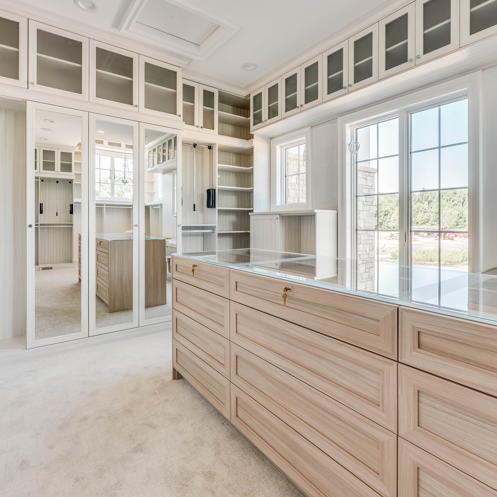 Bright Walk In Closet Luxury Walk In Closet with a window, Island and mirrored doors by California Closets Northern Michigan