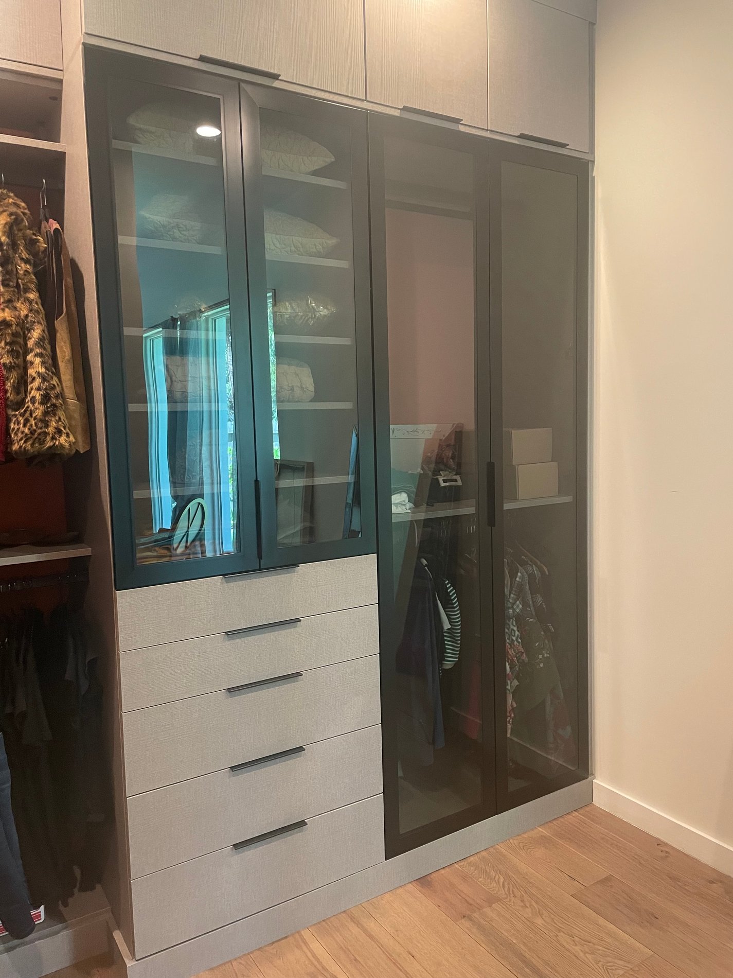 Timeless Wardrobe Walk-In Closet with Corsican Weave & Industrial Black Hardware This elegant walk-in closet combines the luxurious Corsican Weave with industrial black hardware and glass doors.
