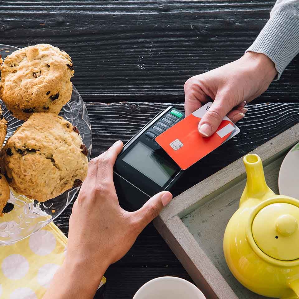Top-down image of a contactless card payment at a counter with tea and scones