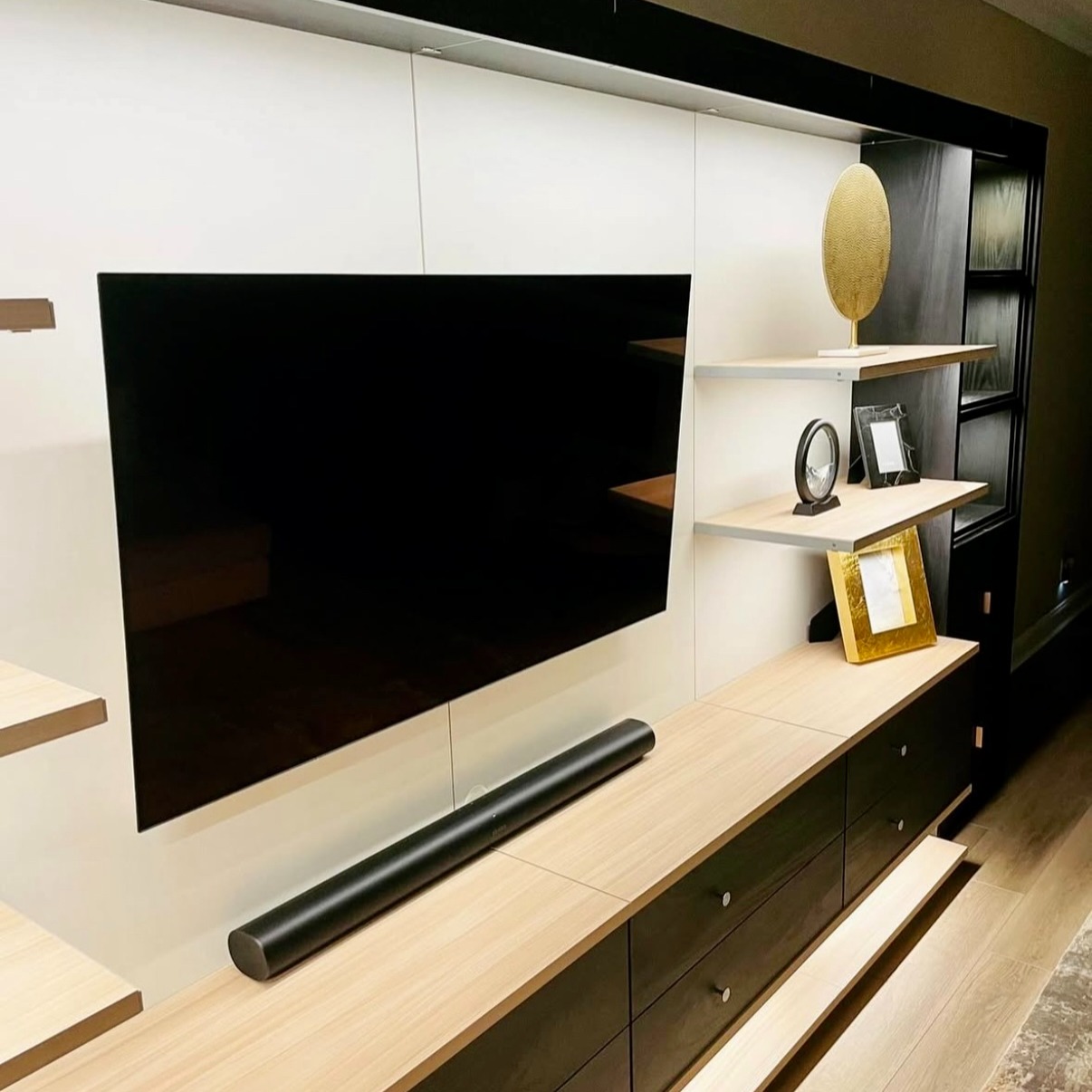 Virtuoso Media Wall & Bookcase in Shadow Black and Cassini Beach Custom Virtuoso media wall and bookcase with Shadow Black drawers, Cassini Beach shelving, and Linen backing, featuring Pub House knurled handles in satin brass and integrated lighting for a modern, sophisticated storage and display solution.