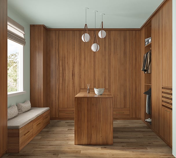 Custom Luxurious Walk-In Closet with Warm Woodgrain Finish | California Closets Austin Luxurious walk-in closet by California Closets Austin, featuring custom wardrobe doors, drawers, bench seating, and a central island for optimal organization and style.
