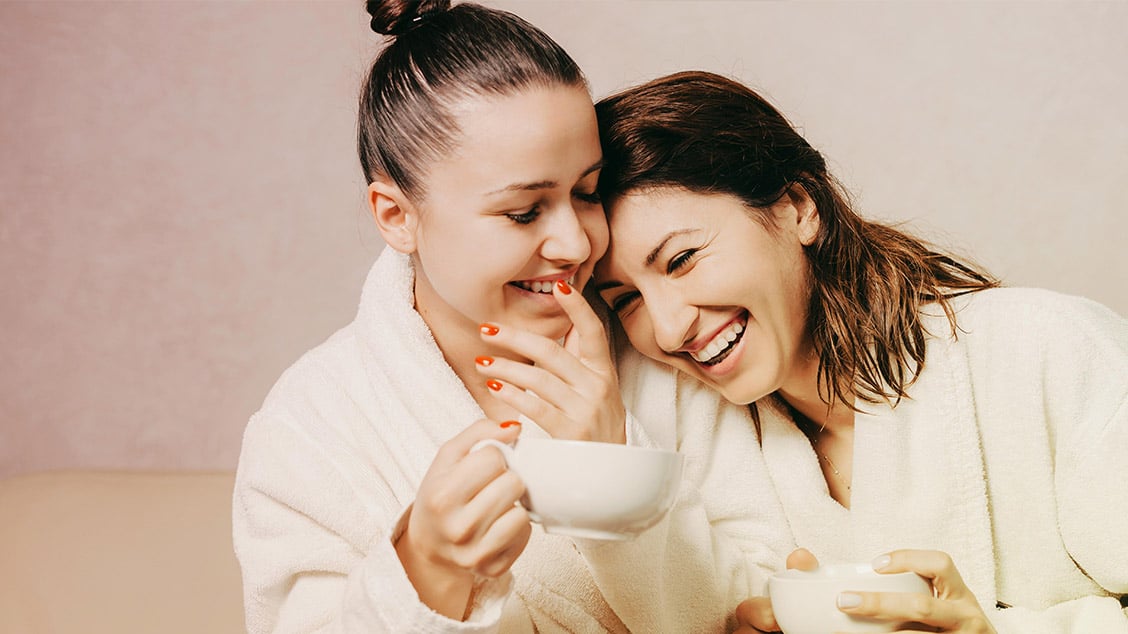 two females in bathrobes, drinking tea.