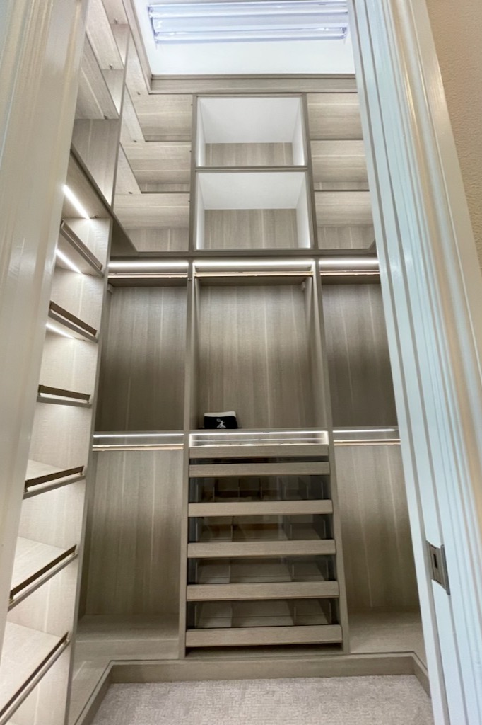 A Master Closet That Marries Luxury & Function Custom master closet in Pietra finish with Linen “Box in a Box” accent trim, gold hardware, recessed straight strip lighting, and Everstyle drawers for shirts, sunglasses, jewelry, and socks in winter leather with gold metal accents.
