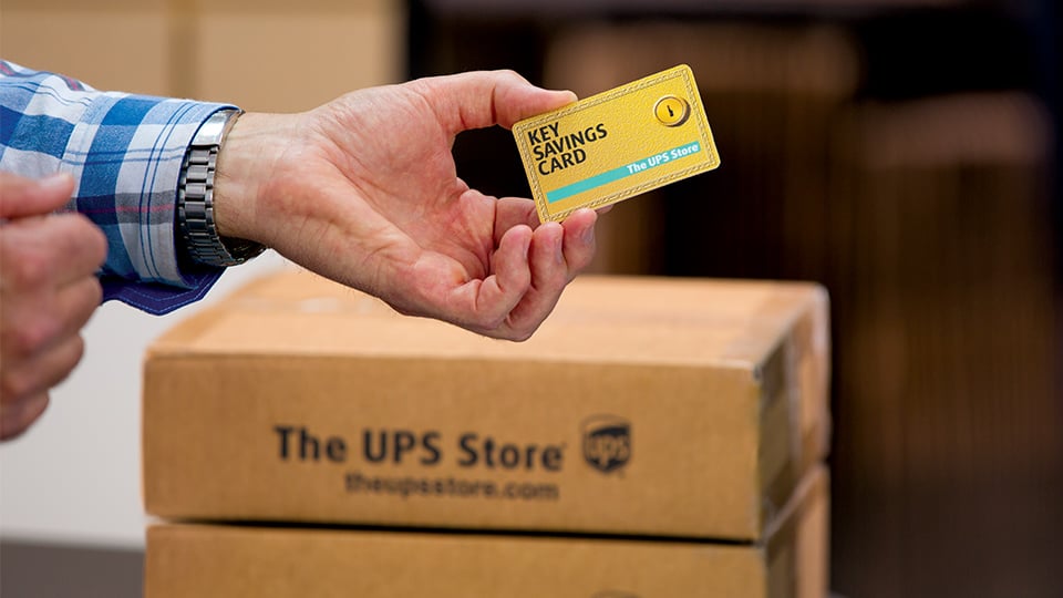 Hand holding a gold The UPS Store plastic card