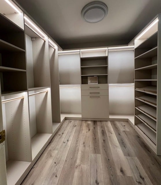 Sophisticated Primary Closet Custom primary closet in linen and stone with gold elite handles and strip lighting.