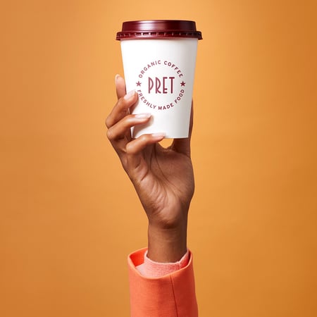Hand holding up a Pret coffee cup