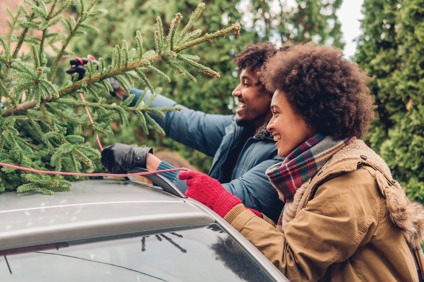 Happy couple loading pine tree on top of car