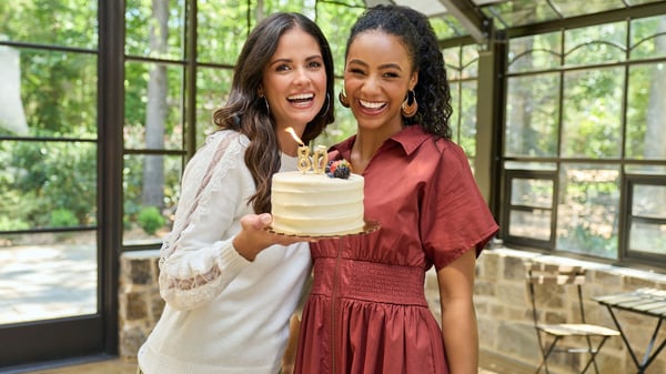 Two women are smiling and holding up an 80th birthday cake.