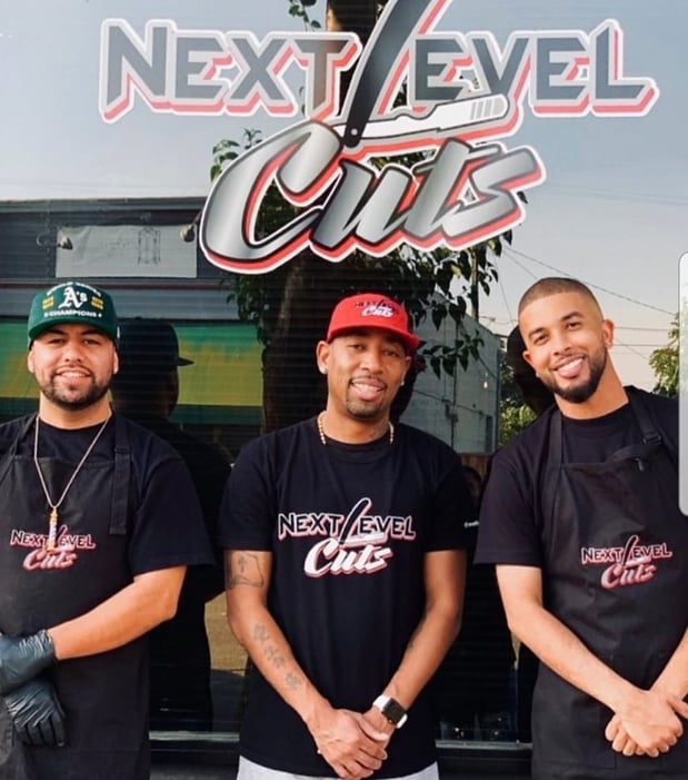 Three men smiling in front of Next Level Cuts business