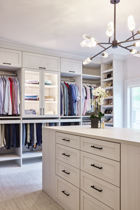Light and Bright Custom Dressing Room Custom light wood finish dressing room with center island, cabinets with lighting, multi-level hanging sections, and slanted shoe shelves.