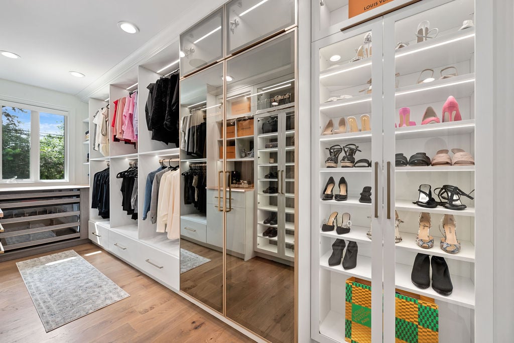 Custom Walk-In Closet Walk in closet with mirrored doors, shaker doors with glass insert, double hang, and a window by California Closets Northern Michigan