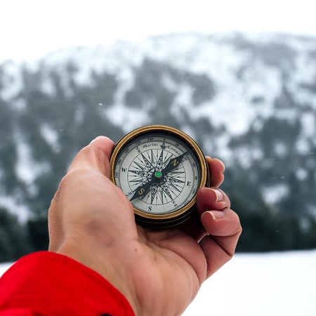 A hand holds a compass in the snowy mountains