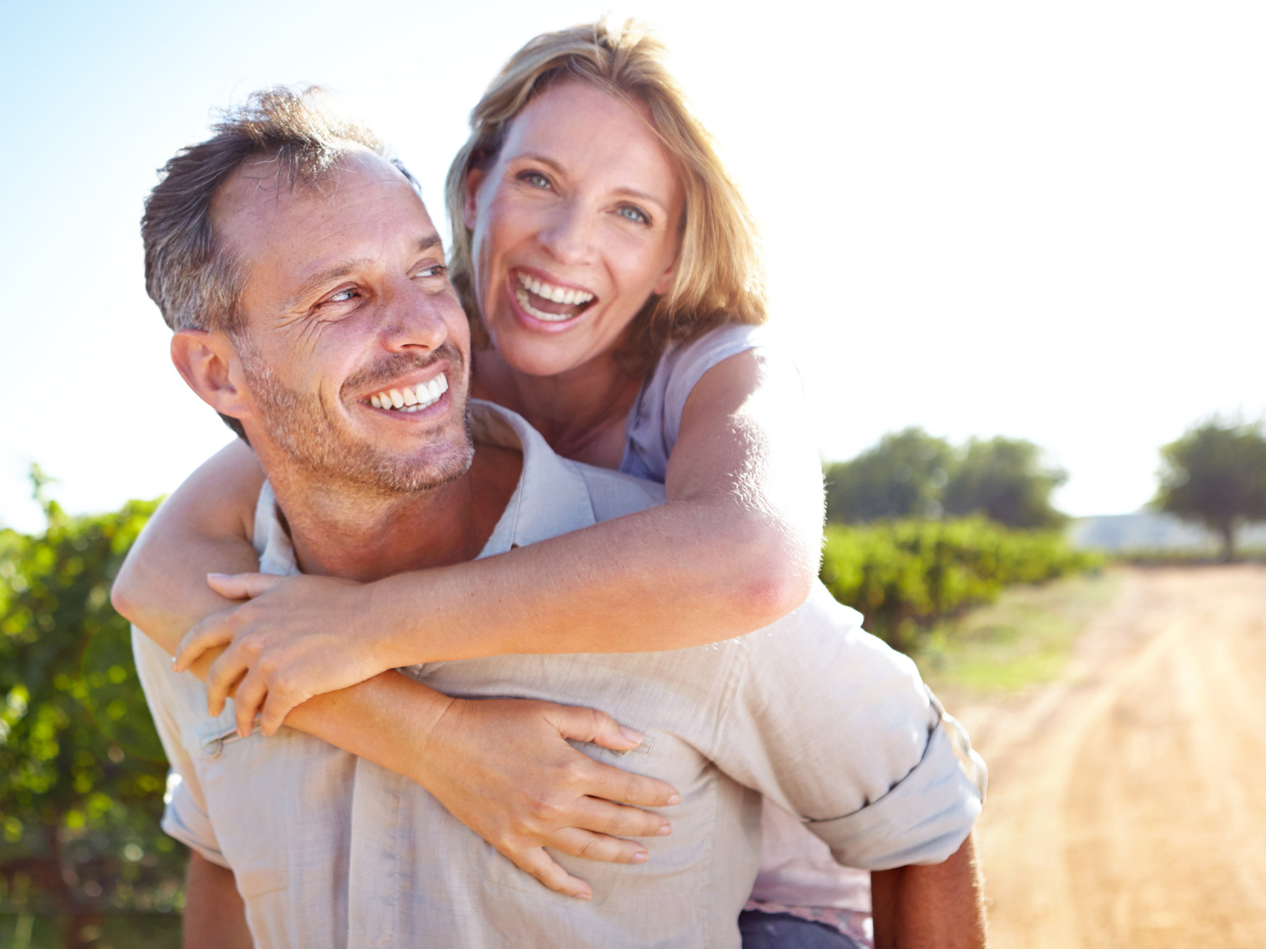 Middle-aged man smiles at his wife as she has her arms wrapped around his shoulders