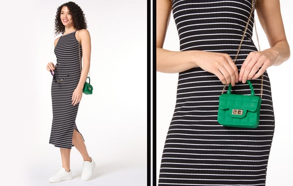 Woman wearing a black and white striped dress is holding a small green purse.