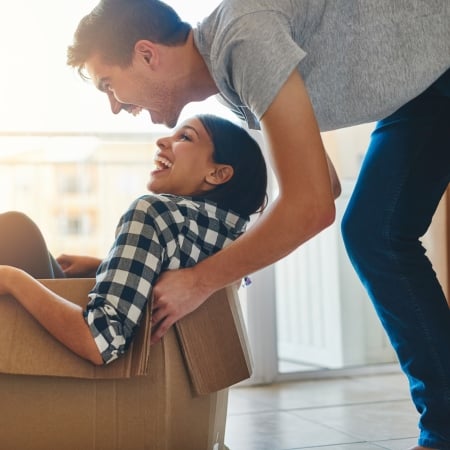 Young man pushes young woman in a cardboard box while moving into a new home.