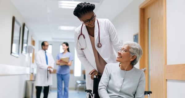 A female doctor pushes an older woman in a wheelchair in a hospital hallway