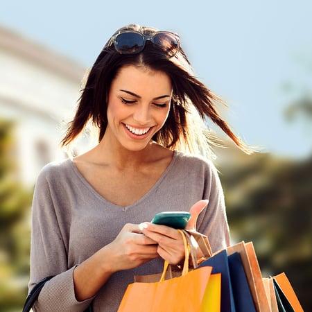 Woman on her phone checking her account with shopping bags in her hand.