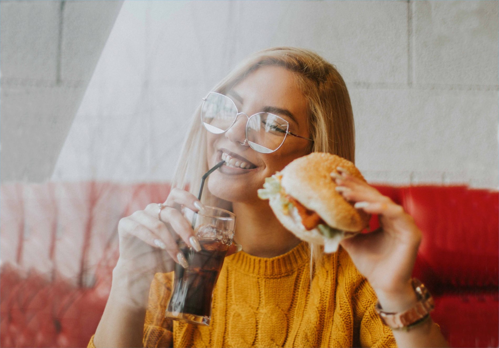 woman drinking a soda and eating a burger