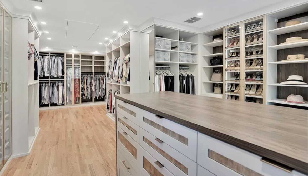 Luxe Dressing Room large walk-in closet with wood floors, white and brown island and hanging and shelves