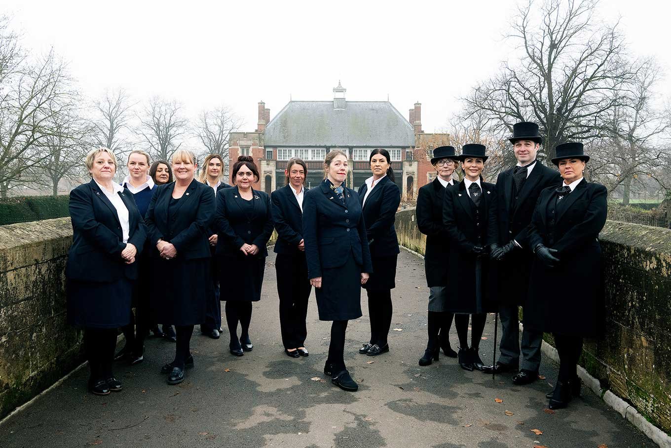 A team of funeral directors and arrangers from Ginns & Gutteridge stand together on a bridge