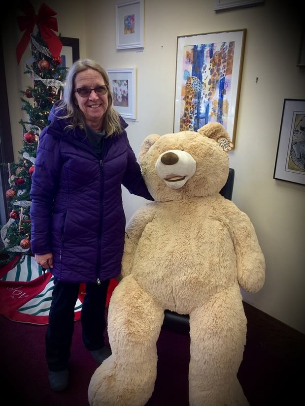 A woman poses with a very large stuffed teddy bear