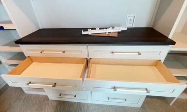 This sophisticated drawer system combines crisp white cabinetry with a rich wood countertop for a striking, modern look by California Closets Virginia Beach. Virginia Beach – Closet storage – White drawer system with dark wood countertop and brushed metal hardware