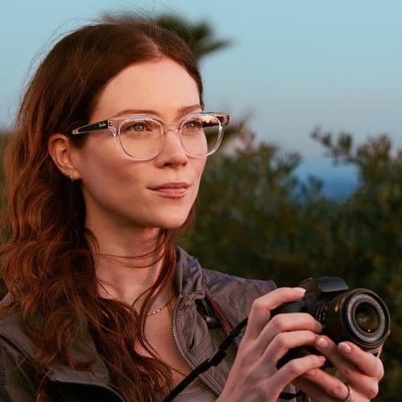 Woman holding a camera while wearing LensCrafters eyeglasses