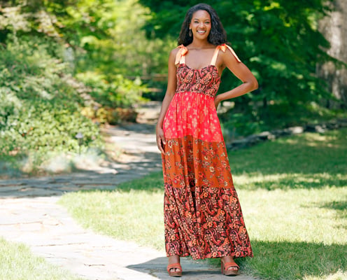 Woman is wearing a red and orange patterned maxi dress from Cato Fashions.