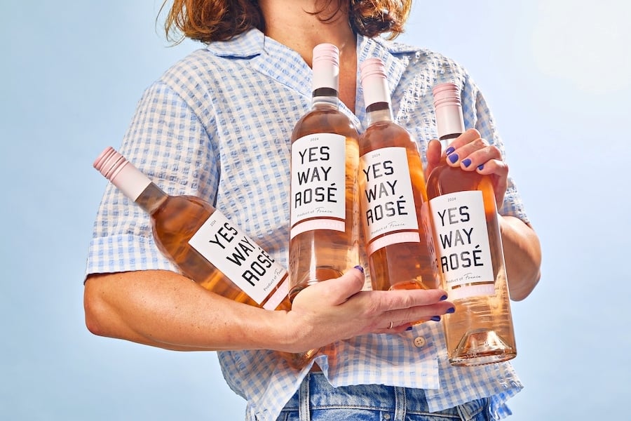 a woman holding four yes way rose wine bottles