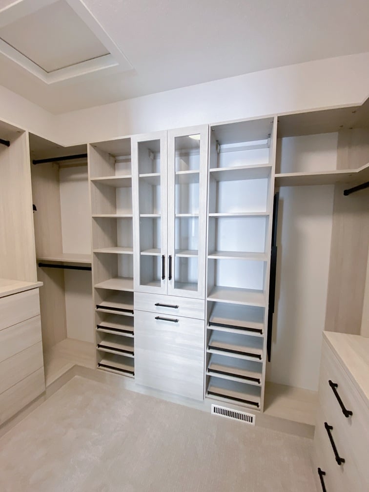 Classic Walk In System Walk in closet in a light natural finish with with glass doors, shoe shelves, tilt out hamper, and drawers.