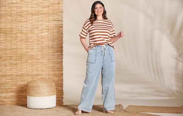 Woman is wearing a plus size striped top and wide leg jeans.