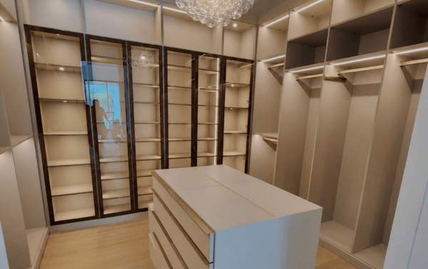 Luxury Woman's Walk-In Closet Custom Walk-In Closet Dressing Room with Center Island Shoe Shelving Display Light Wood Cabinetry Drawer Storage.