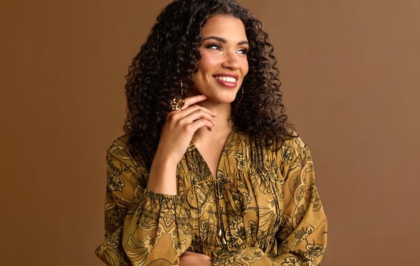 Woman is wearing a green v neck blouse and gold jewelry