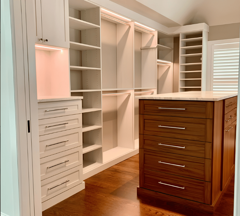 Two-toned Primary Walk-in Closet Light wood closet with center island in a walnut finish and marble countertop