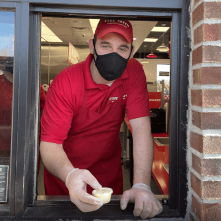 An employee at the Hoxsie Five Guys in Warwick, Rhode Island, hands a customer a condiment cup through the store's mobile pickup window.
