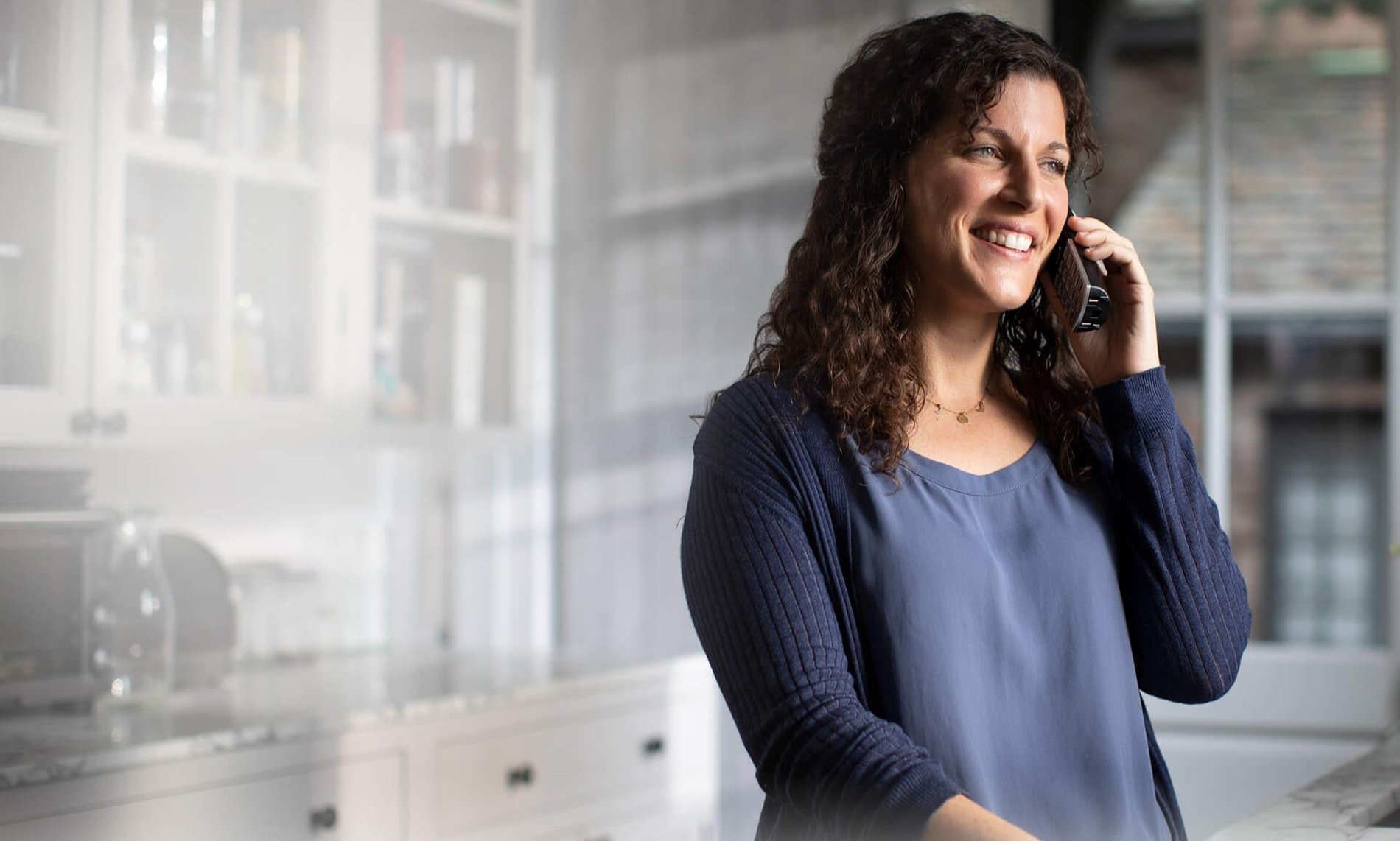 Photo of woman standing in a kitchen talking on a cordless phone using an Optimum Voice connection