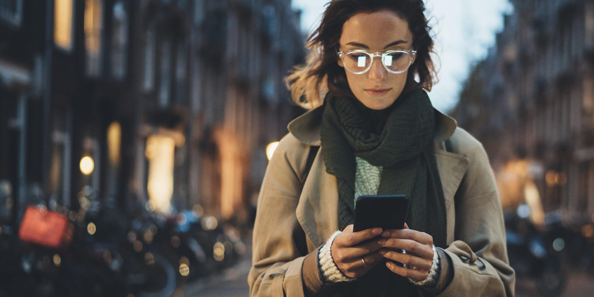 Photo of young woman looking at her Optimum WiFi Hotspot connected phone while walking on a city street