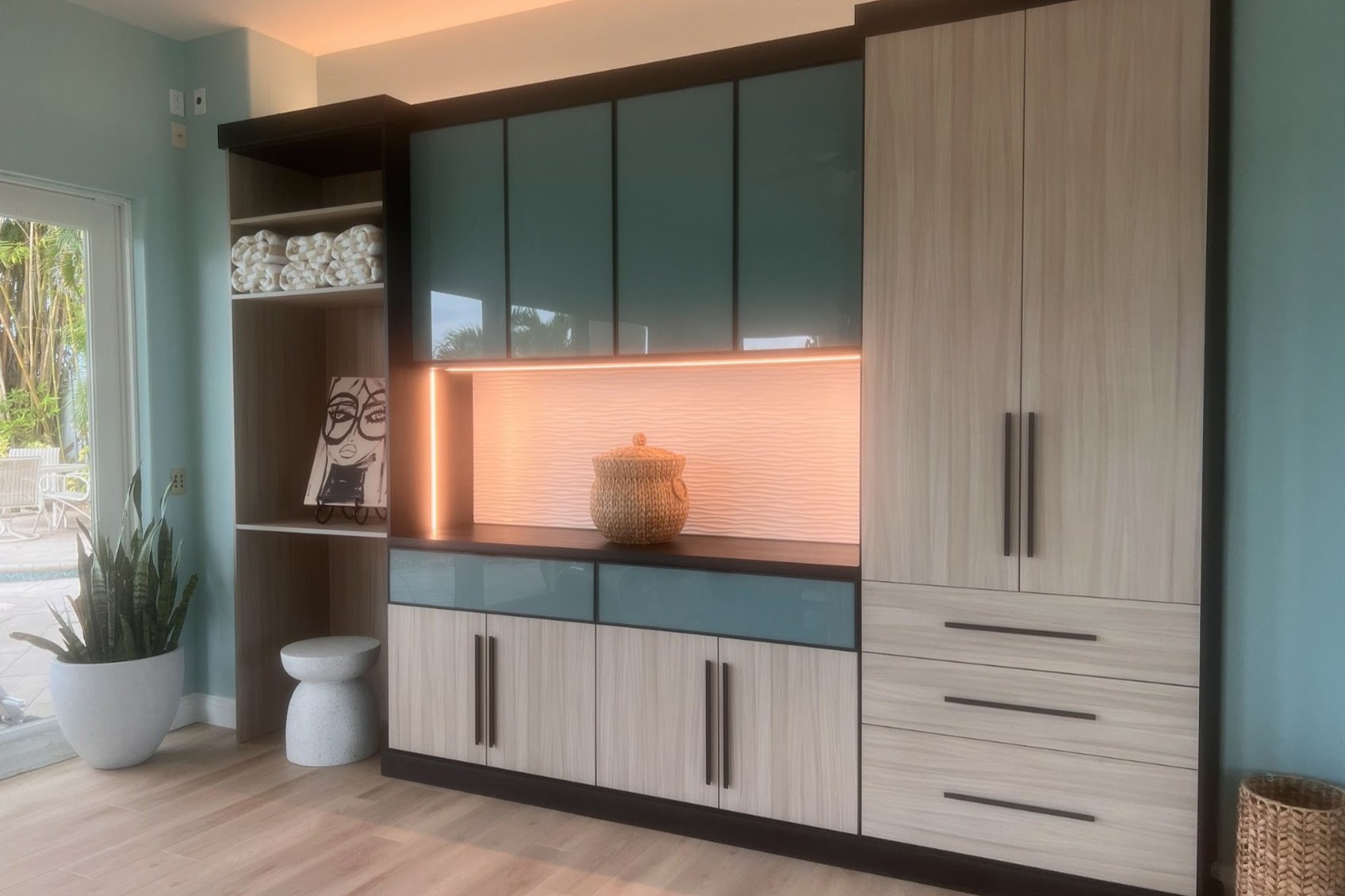 Modern Built-In Storage Modern custom built-in with wood-grain and colored cabinetry, illuminated open shelving, drawers, and floor-to-ceiling storage.