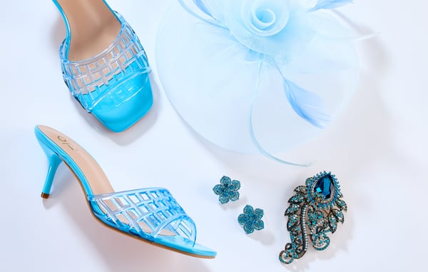 A blue floral fascinator, blue jelly kitten heels, blue floral stud earrings and a blue brooch are artfully displayed on a white background.