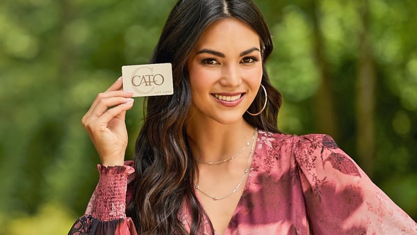 Woman is smiling and holding up a Cato Fashions gift card.