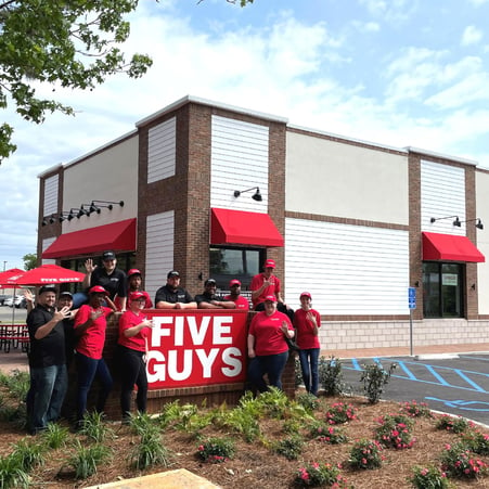 Employees pose for a photograph around the exterior sign in front of the new Five Guys restaurant at 241 South Greeno Road in Fairhope, Alabama.