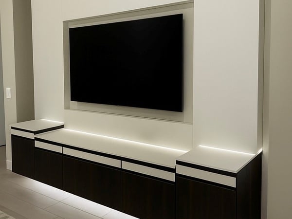 A sleek floating entertainment center creates a clean, architectural focal point with streamlined cabinetry, integrated lighting, and concealed storage beneath a wall-mounted television. Modern floating entertainment center with dark cabinetry, wall-mounted television, concealed storage, and integrated lighting.
