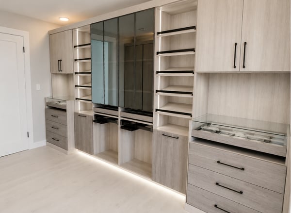Luxury custom walk-in gallery closet designed by California Closets South Palm Beach in Florida, featuring glass-front cabinetry, integrated lighting, angled shoe shelving, jewelry drawer organizers, and elegant modern finishes. Custom walk-in closet by California Closets South Palm Beach FL with glass doors, built-in lighting, shoe shelves, and jewelry storage designed by Sybil Archambault