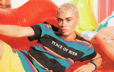 A male model poses on a pool float in a graphic tee shirt and swim trunks.