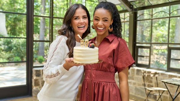 Two women are smiling and holding up an 80th birthday cake.