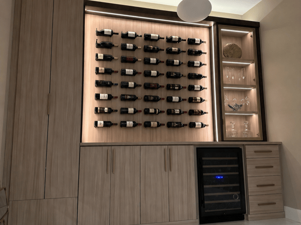 A sophisticated custom wine wall designed to turn a collection into a statement, with integrated bottle storage, illuminated display shelving, concealed cabinetry, drawers, and a built-in wine refrigerator. Custom wine storage wall with illuminated bottle display, built-in cabinetry, drawers, shelving, and wine refrigerator.