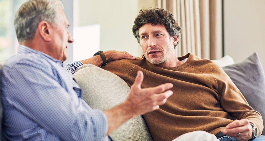 Two men have a conversation while sitting on a couch.