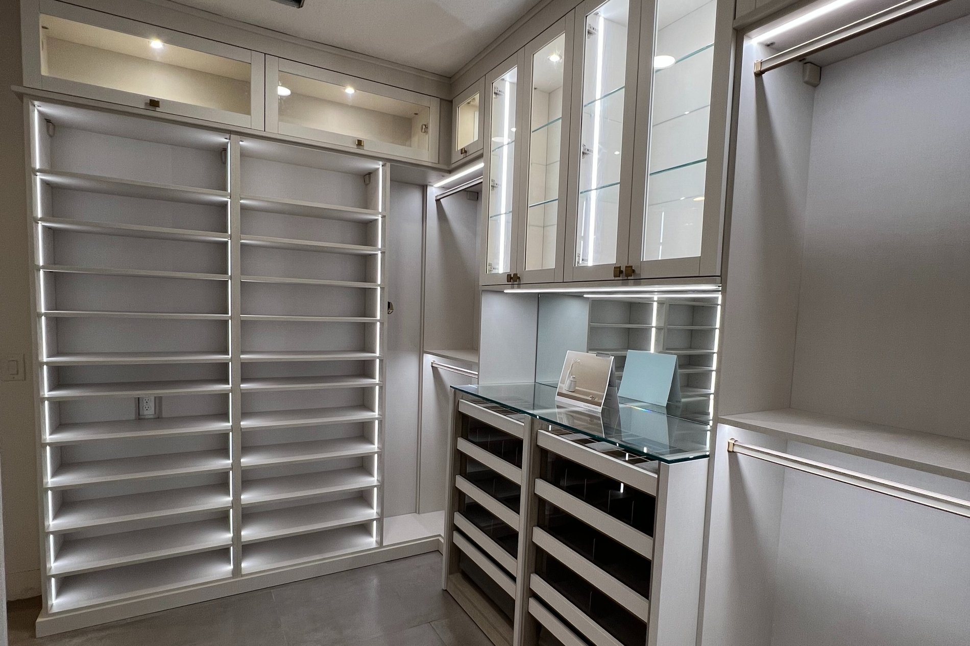 Elegant Walk-In Closet in Linen and Pietra with Gold Accents and Mirror Flip-Up Doors Walk-In closet in Linen and Pietra with Lighting, Gold Shaker Glass, Everstyle drawers, Glass Counter Wrap panels and Mirror Flip up doors